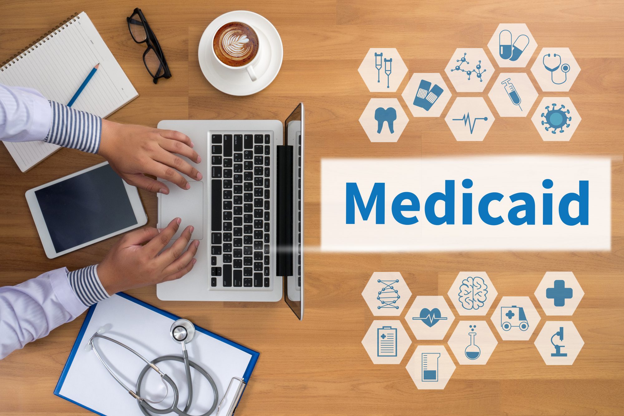 Person using a laptop at a desk with a notebook, tablet, coffee, stethoscope, and healthcare icons. The word "Medicaid" is prominently displayed, highlighting the importance of healthcare planning in LaGrange.