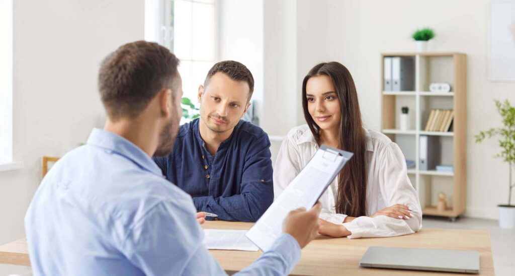 A man holding a clipboard speaks to a seated couple across the table in a modern office setting, offering insights from LaGrange estate planning attorneys.