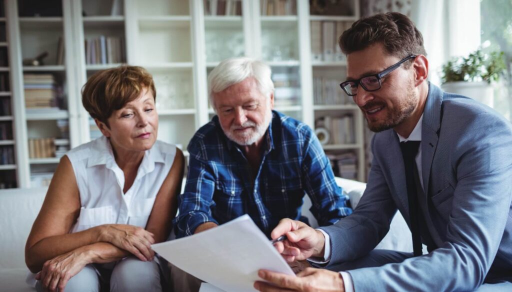 Three people sit on a couch, reviewing a document together. A man in a suit discusses Western Springs Estate Administration with an older couple. Shelves filled with books are visible in the background, adding to the atmosphere of earnest focus and thoughtful planning.