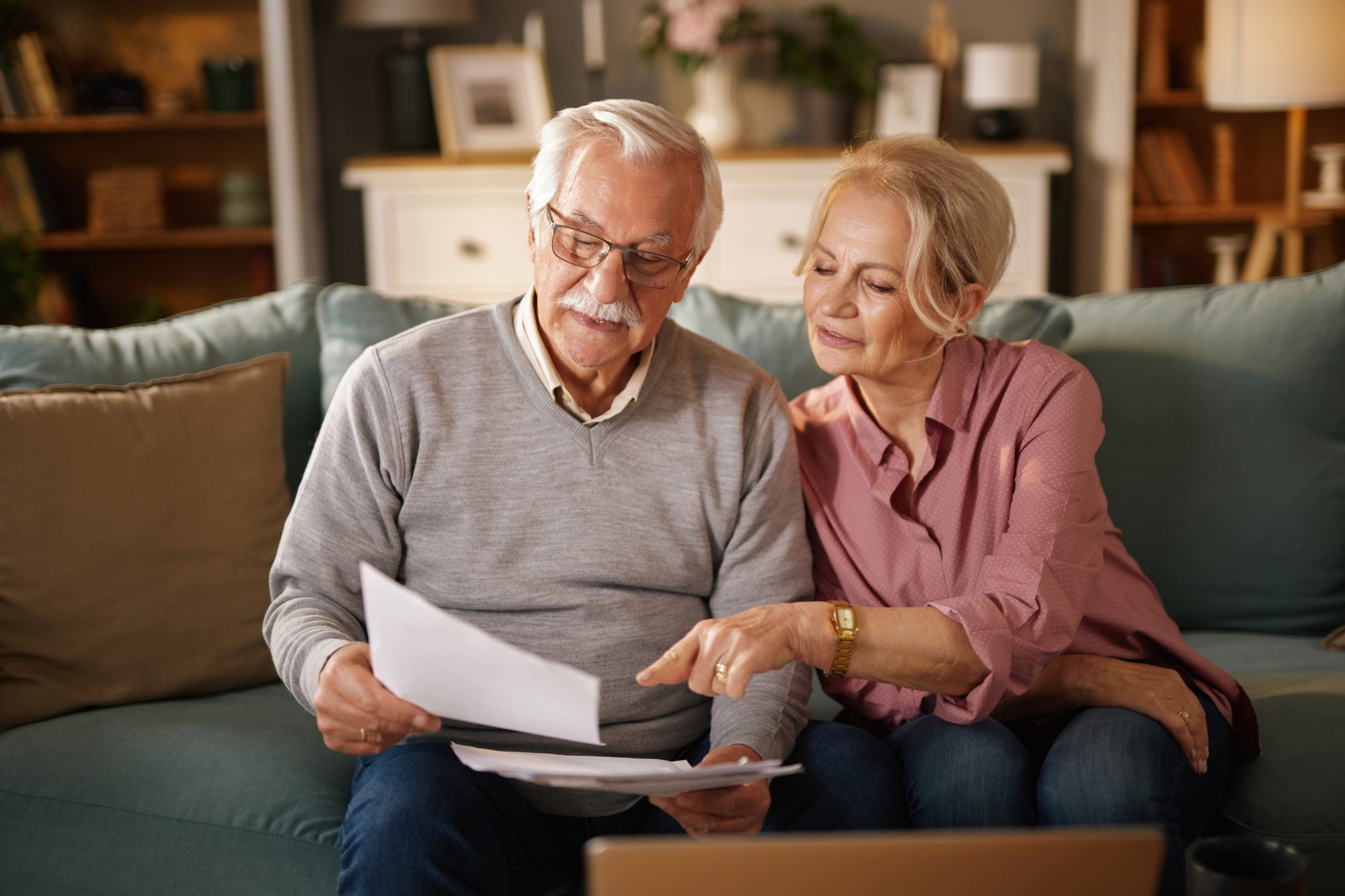 An older man and woman sit on a couch reviewing documents for their will and needing help from Westchester Estate Planning Lawyer.