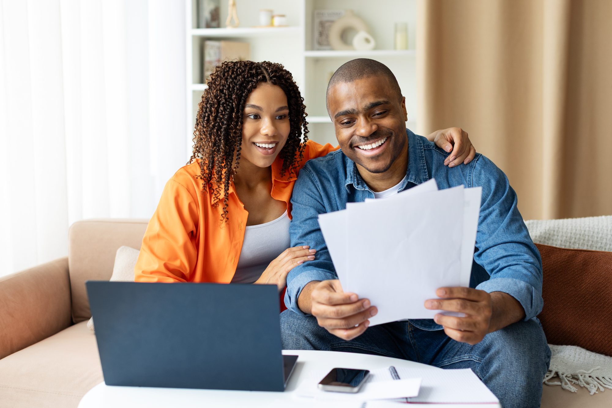 A smiling couple sits on a couch with a laptop, holding documents and appearing pleased while reviewing paperwork together, likely after consulting a LaGrange probate attorney.