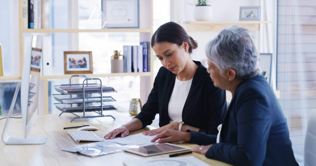 Two women in business attire sit at a desk reviewing documents with LaGrange estate planning lawyers in a modern office setting.