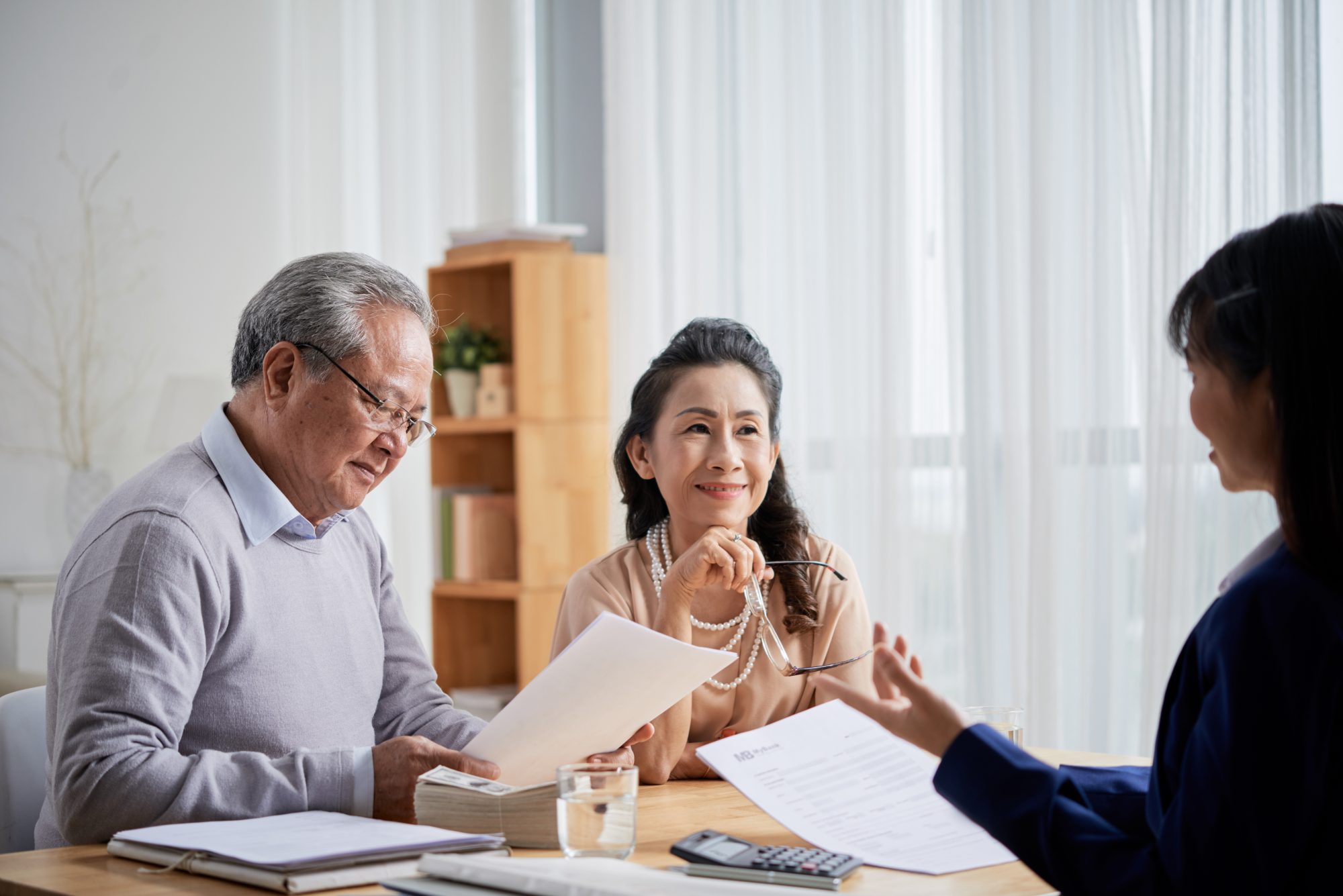An older couple sits at a table reviewing documents and talking with a professional woman in an office setting.