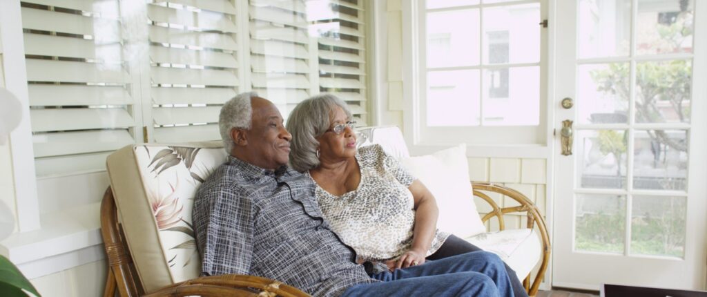 An older couple sits closely together on a couch in a sunlit room, looking out the window with relaxed expressions, feeling confident after meeting with Brookfield estate planning lawyers.