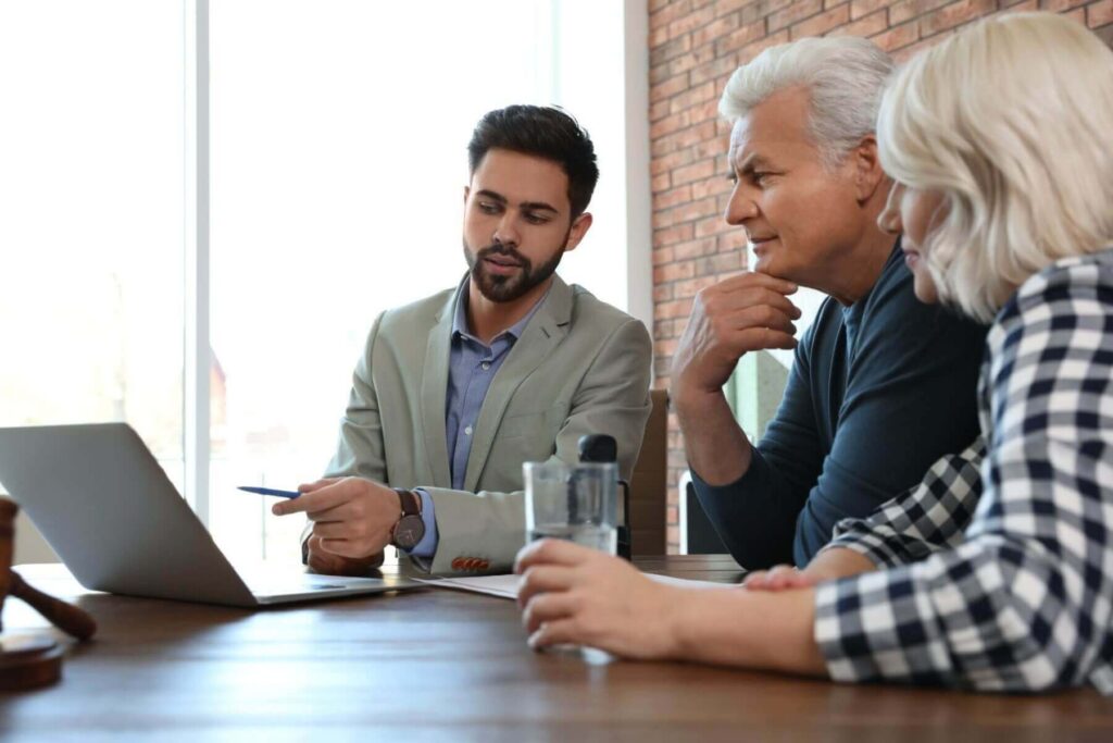 Three people sitting at a table, engaging in discussion about LaGrange Park Trusts with a laptop open. The man in a suit gestures with a pen while the other two listen attentively.