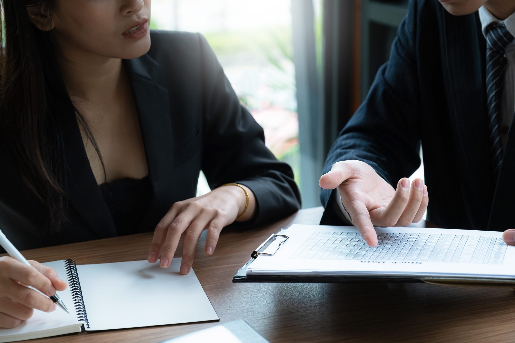 Two people in business attire sit at a table, one writing in a notebook while a Valparaiso estate planning attorney points at a document on a clipboard.