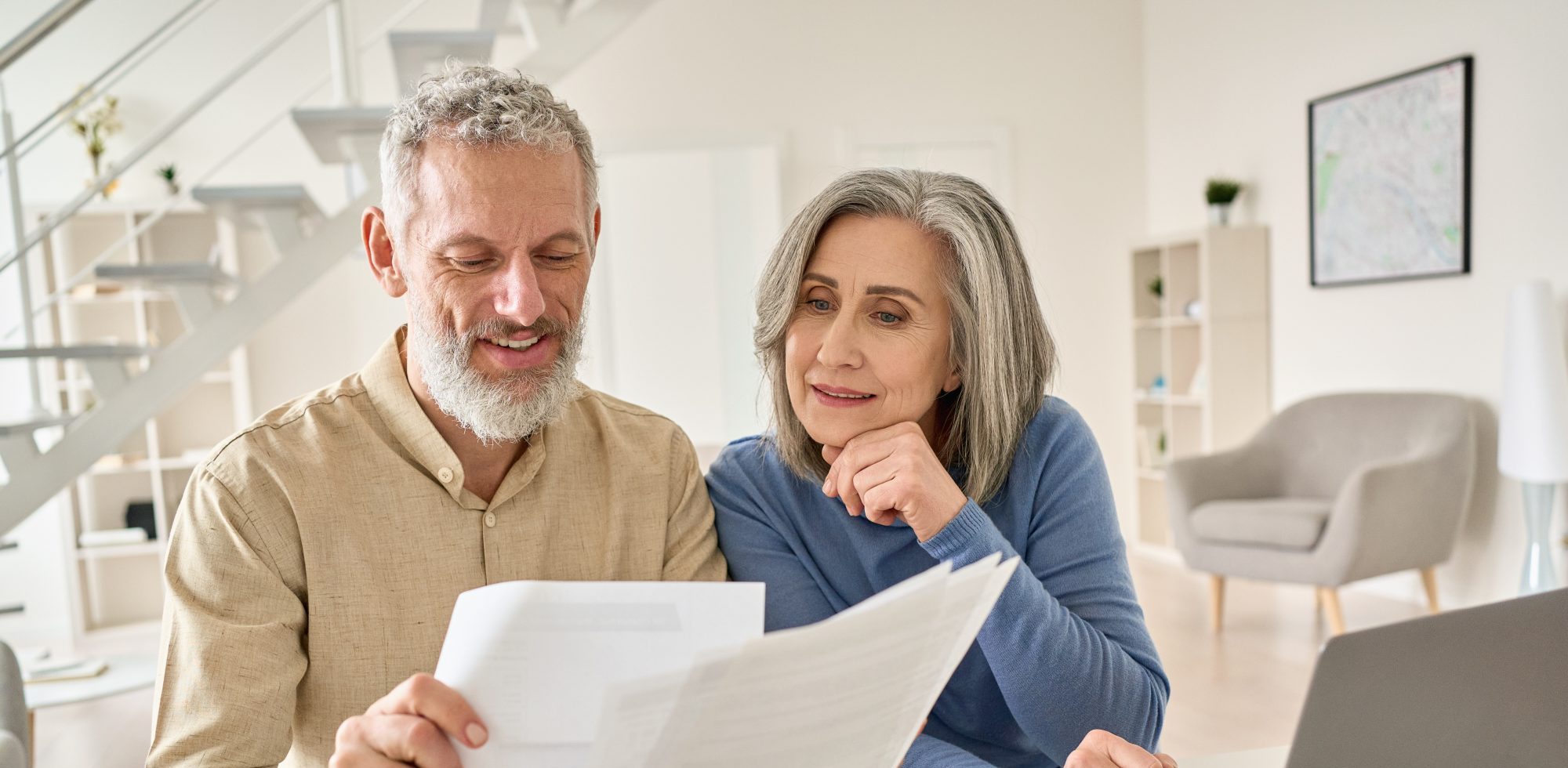 An older couple sits at a table reviewing documents with a Deerfield estate planning lawyer via laptop in their bright, modern living room.