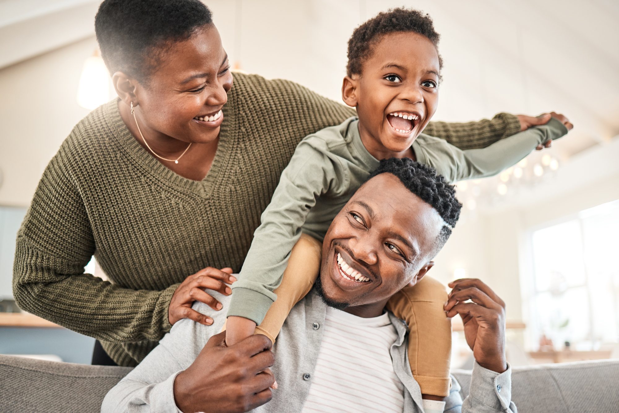 A smiling family, with a man carrying a child on his shoulders and a woman standing beside them, all indoors in their LaGrange Park home, discussing LaGrange Estate Planning.