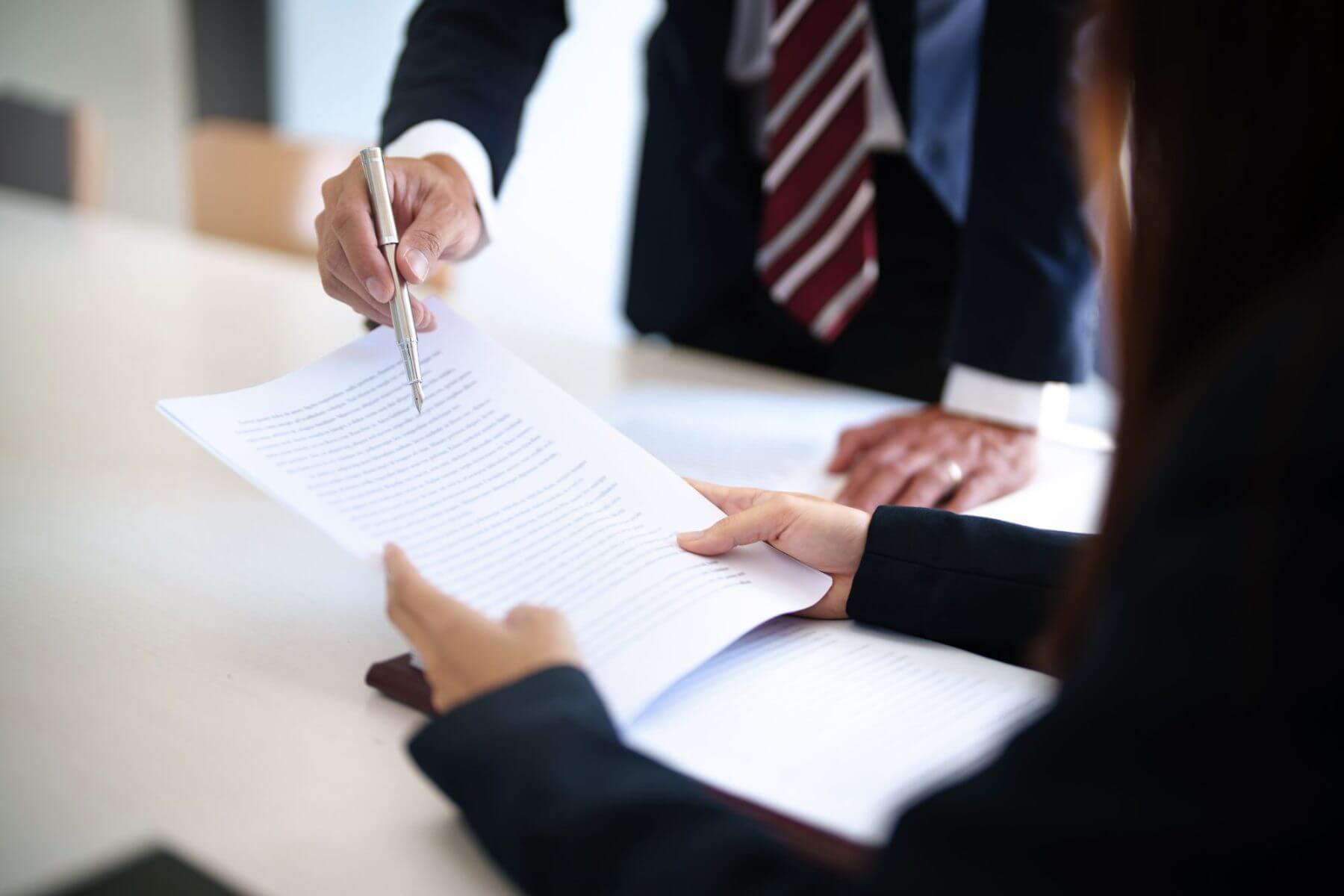 Two people review a document at a table. One person points with a pen while the other holds the papers, discussing details of Brookfield Elder Law. Both dressed in business attire, only their hands and arms are visible.
