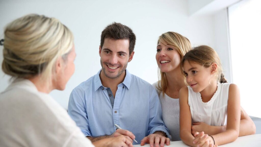A family of three, two adults and a child, sit at a table engaged in conversation with a woman. The man holds a pen as they discuss their future plans with the guidance of LaGrange Estate Planning.