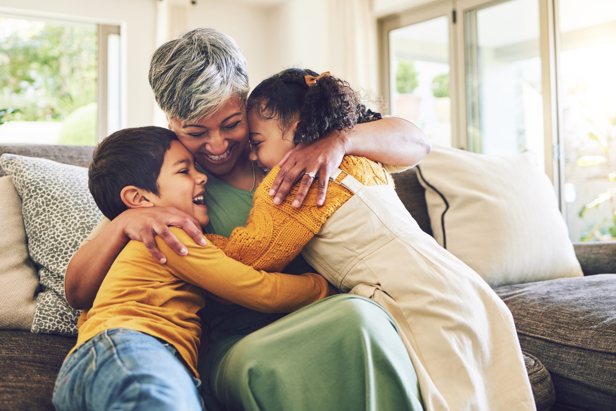 An elderly woman sits on a couch, embracing a young boy and girl, all beaming in their casual clothes. Their joyful gathering reflects the warmth often celebrated at Western Springs Estate Administration.