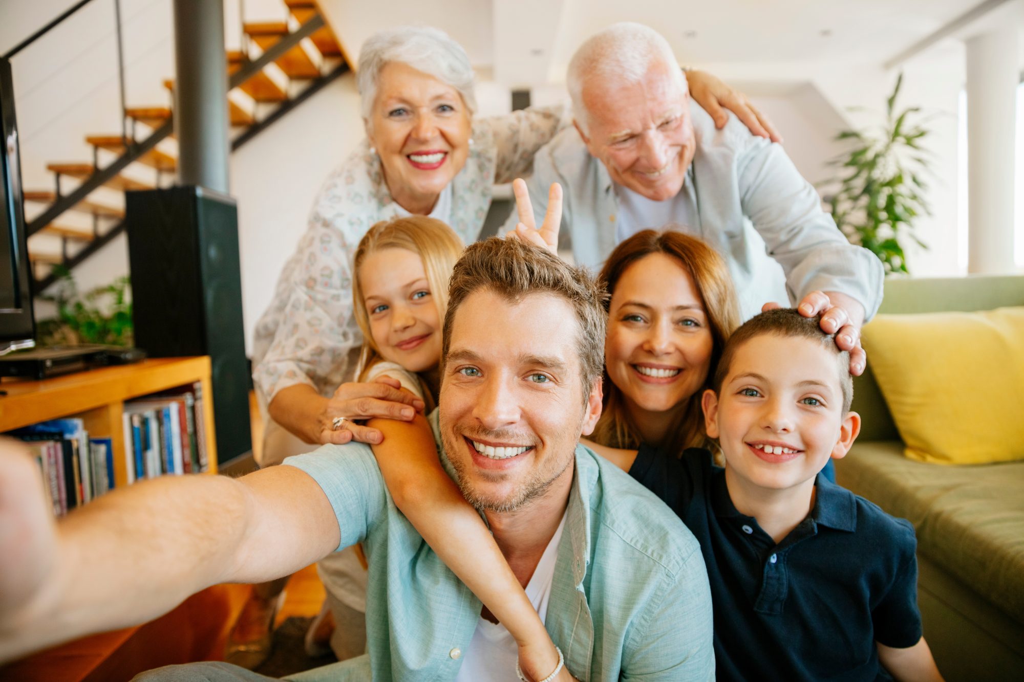 Three adults and two children smile at the camera for a group selfie in a bright living room. An elderly couple stands behind a younger family of four, highlighting the importance of planning with a wills and trusts attorney LaGrange.