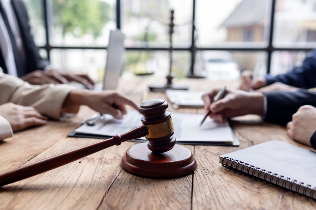 A wooden gavel on a table with people in reviewing documents, when establishing a trustee for trust work with LaGrange Trusts Lawyer.