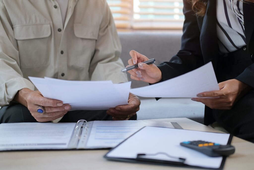 Two people review documents together; one holds a pen, focusing on LaGrange Estate Planning. A binder and calculator are on the table, essential tools for organizing financial affairs effectively.