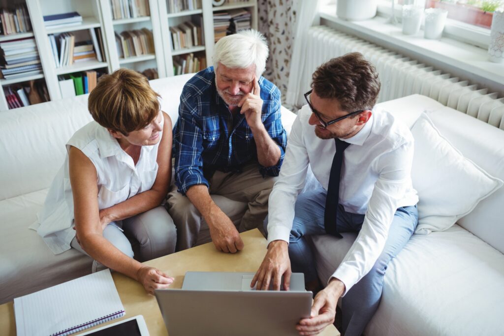 Three people sit on a couch looking at a laptop, focused on LaGrange Estate Planning. A man in a shirt and tie points at the screen, while the other two, a man and woman, attentively watch. Shelves with books are in the background.
