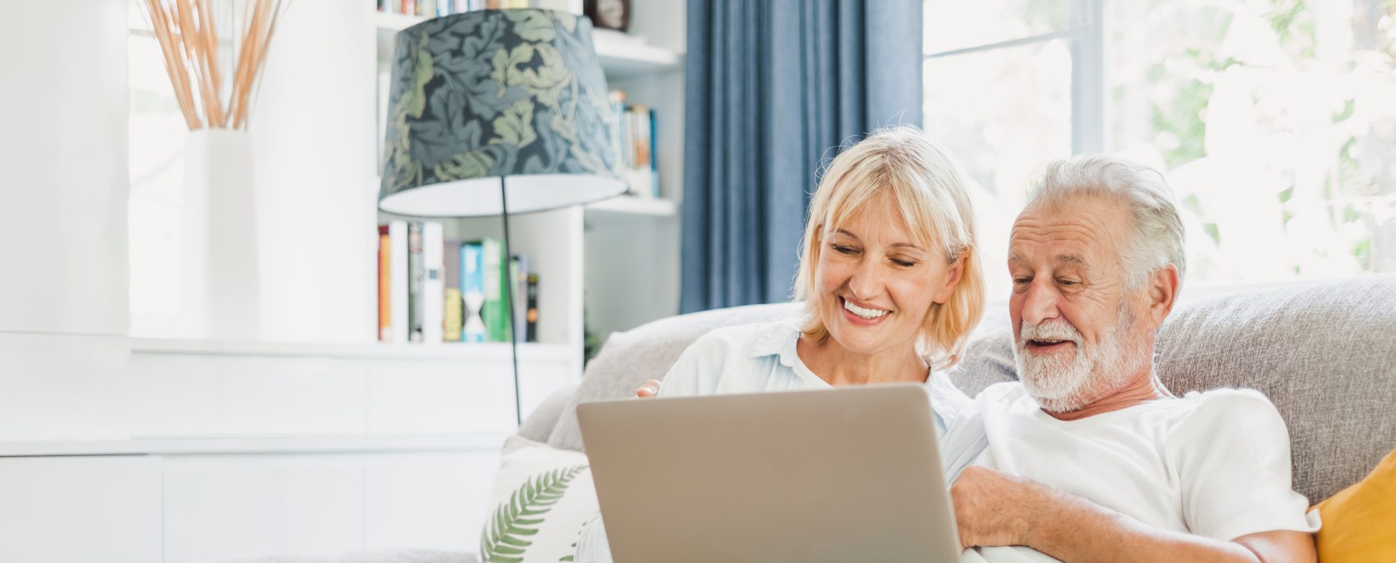 An older couple sits together on a couch, smiling and looking at a La Grange Estate Planning newsletter.