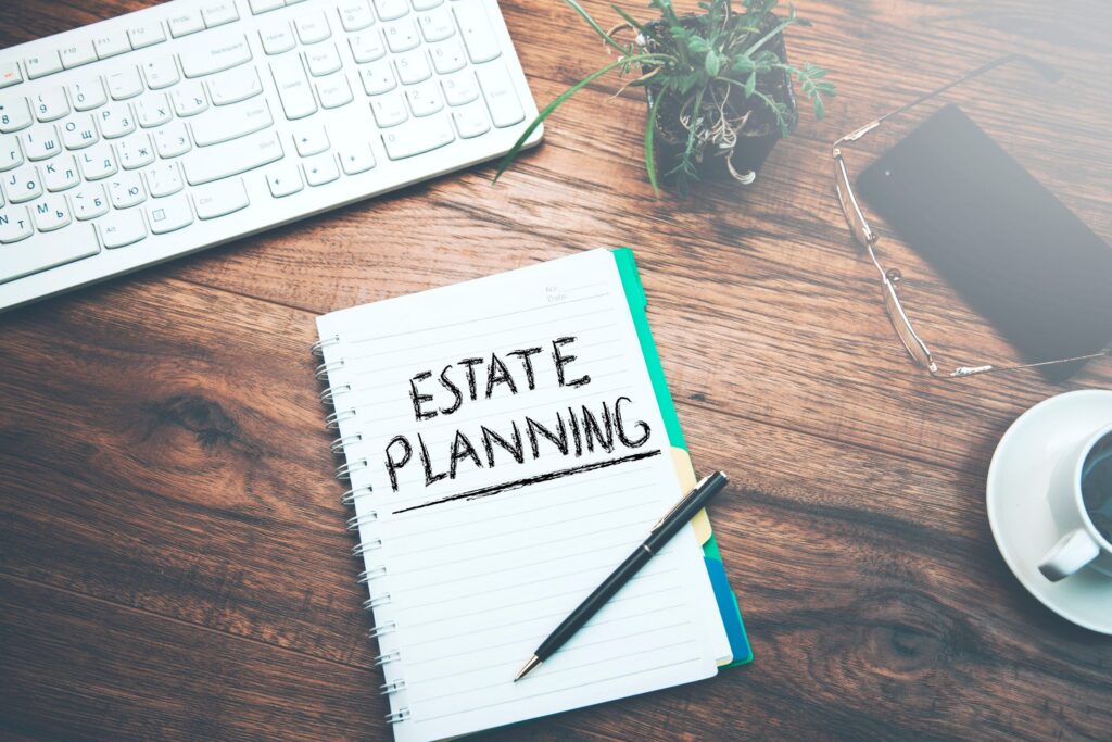 A notebook with "Estate Planning" lies on a wooden desk beside a keyboard, plant, smartphone, glasses, and a cup of coffee—an ideal setup for diving into LaGrange Estate Planning insights.