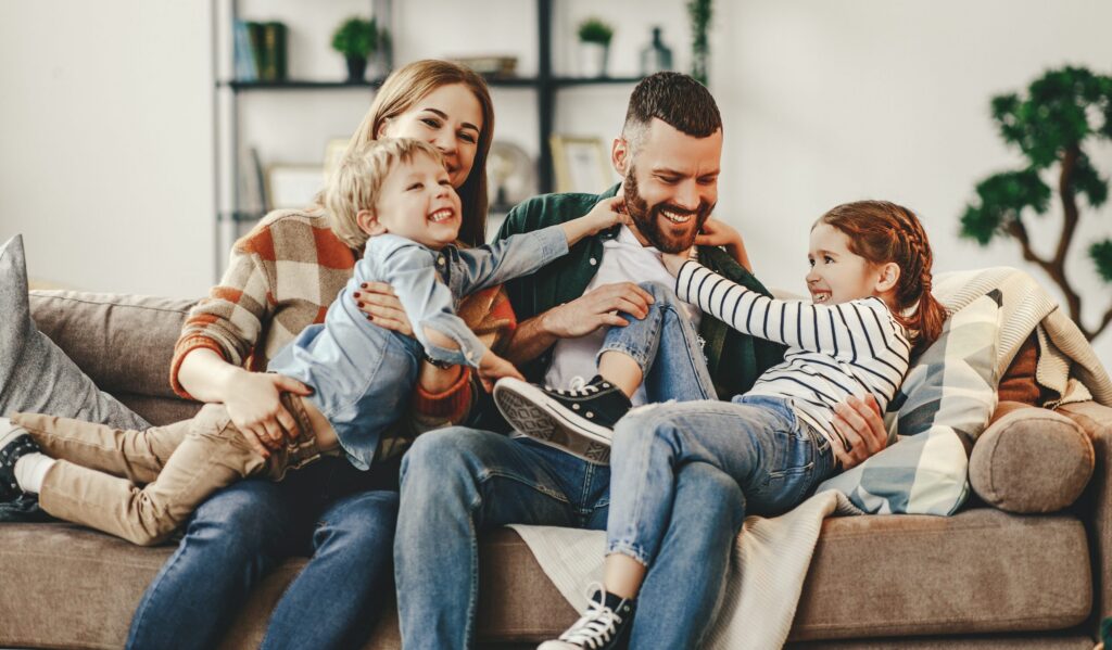 A family of four sits on a sofa, joyfully interacting in a living room adorned with shelves and plants, demonstrating the warmth that thoughtful Brookfield Elder Law can provide.
