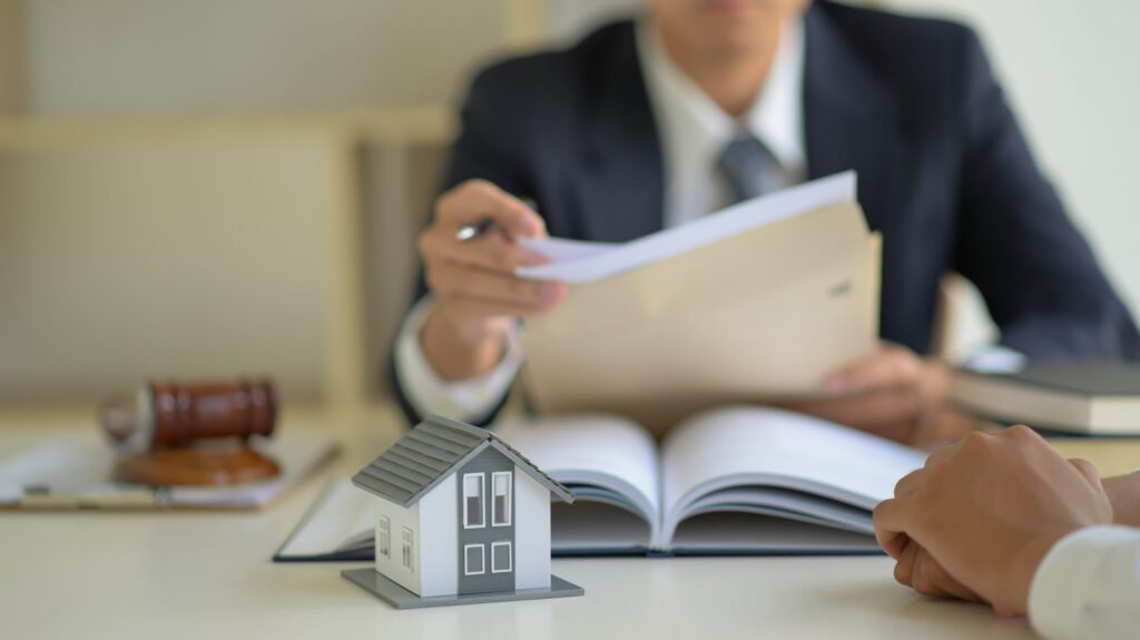 A person in a suit reviews documents at a desk adorned with a model house and gavel, possibly discussing LaGrange Estate Planning or real estate legalities.