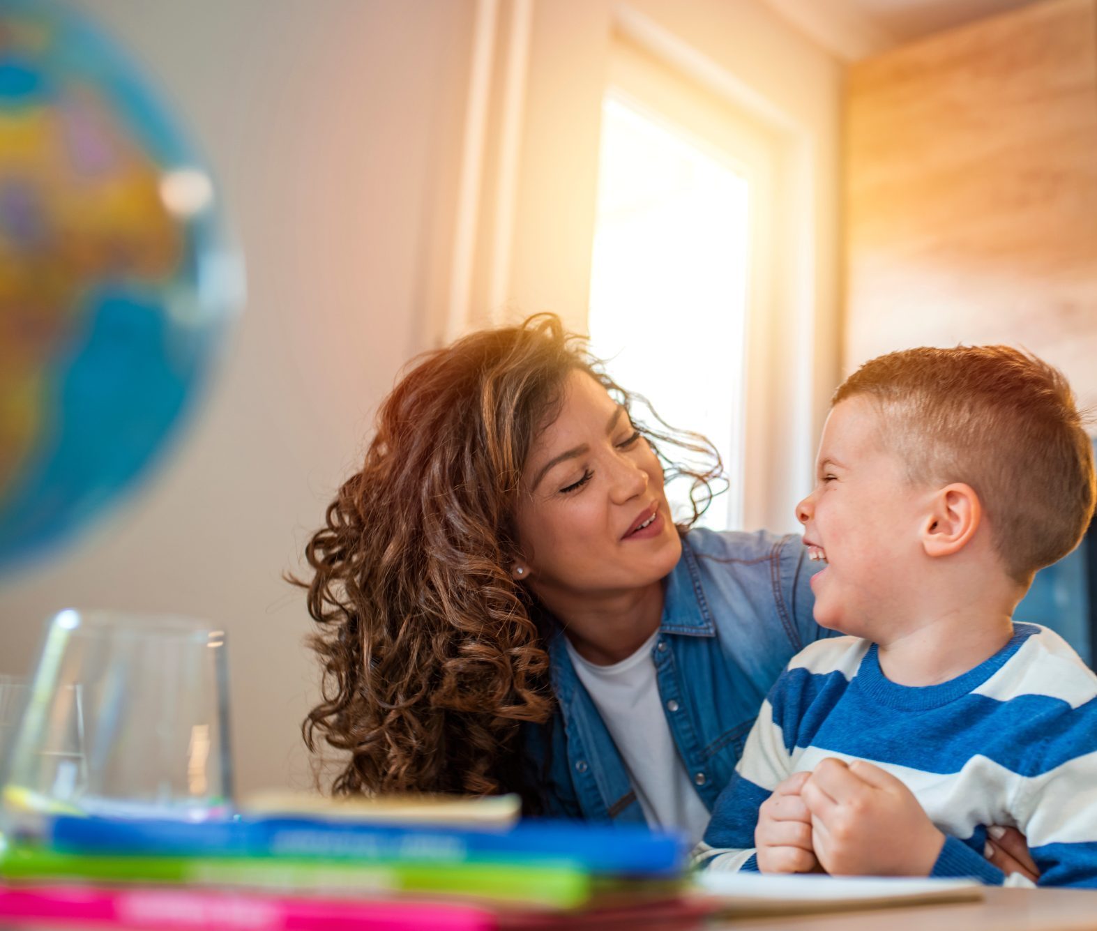 A woman who has done Deerfield Special Needs Planning and a young boy sit together at a table in a bright room, smiling at each other.