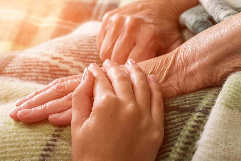 Close-up of a younger hand gently holding an older hand, both resting on a plaid blanket, symbolizing the compassionate care and support often navigated with expertise in Brookfield Elder Law.