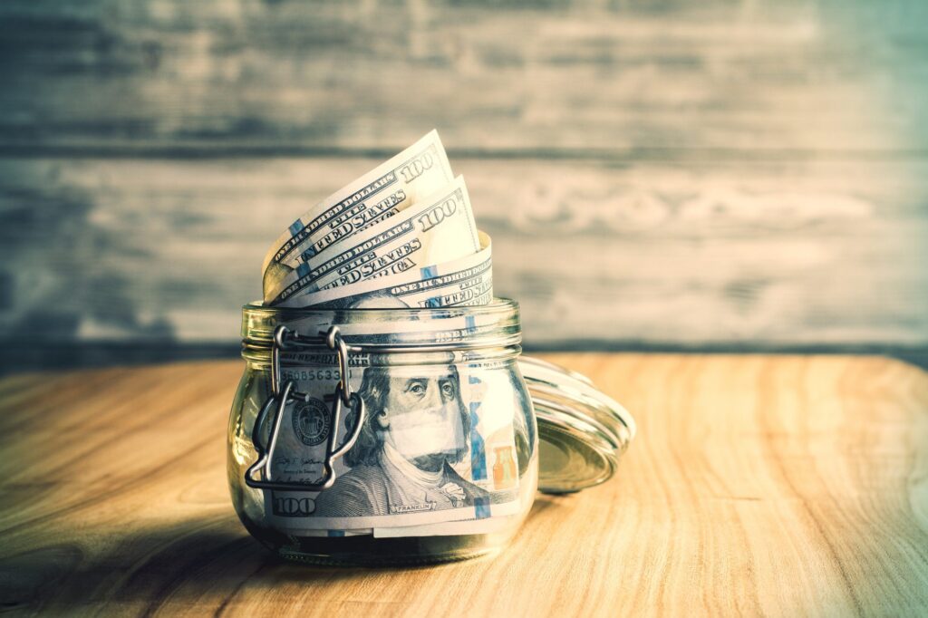 A jar filled with rolled U.S. hundred dollar bills secured with a padlock rests on a wooden surface, symbolizing the foresight and security emphasized in LaGrange Estate Planning against a blurred background.