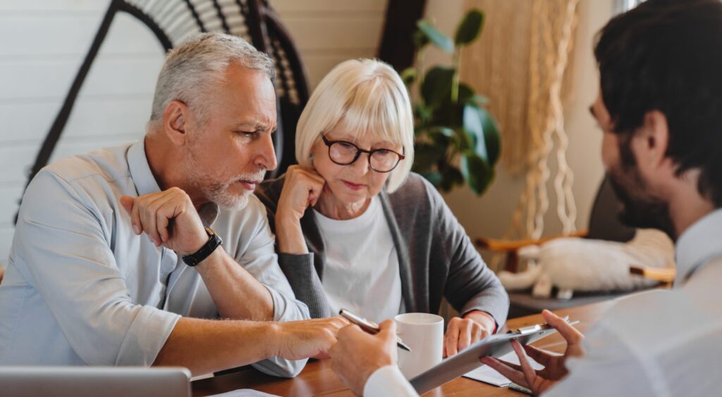 An older couple sits at a table reviewing documents and a digital tablet with a professional in an office setting listening to an estate planning attorney in La Grange.